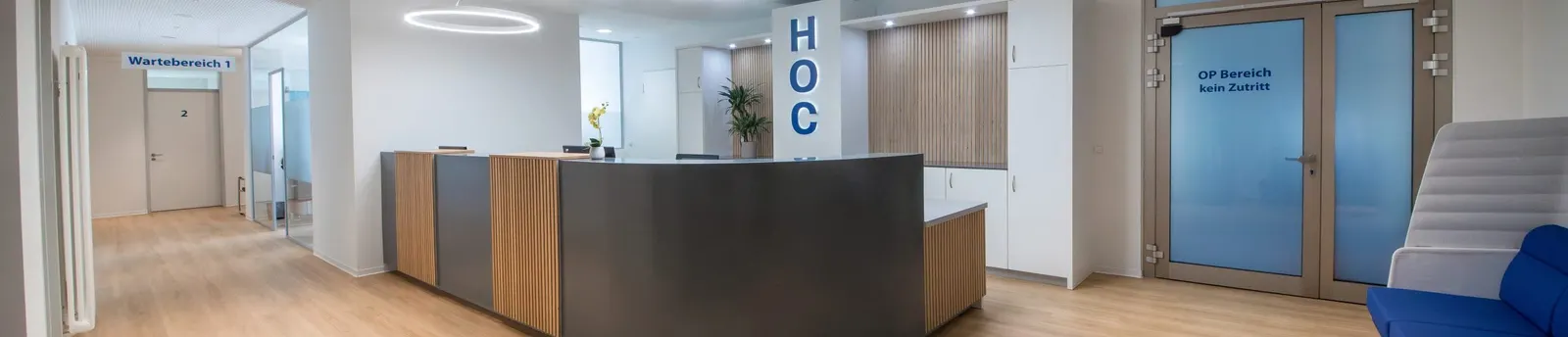 Empfangsbereich der Praxis HOC mit Tresen, im Hintergrund das Schild Wartebereich 1